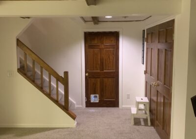 Basement hallway with wood paneled doors, stair railing, and carpet flooring