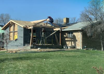 Workers framing a roof addition on a brick house with house wrap installed