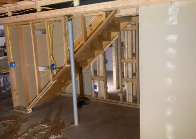 Basement framing under construction with stairs, wiring, and drywall installation