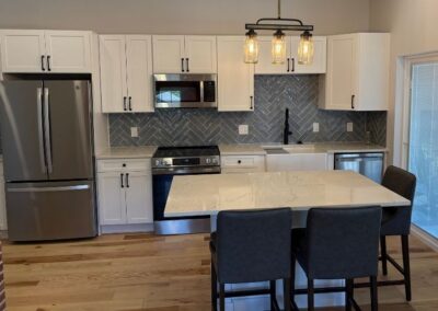 Remodeled kitchen with white cabinets, herringbone tile backsplash, and mason jar pendant lighting