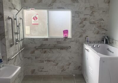 Accessible bathroom with curbless walk-in shower, wall-mounted sink, and stacked washer and dryer