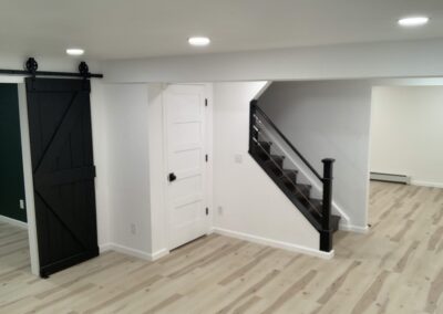 Finished basement with black sliding barn door and black stair railing over wood-look flooring