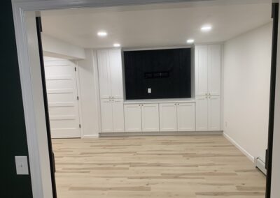 Finished basement media wall with white built-in cabinets and dark accent wall for TV