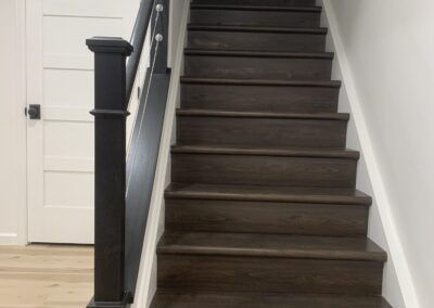 Basement staircase with black railing and wood-look stair treads