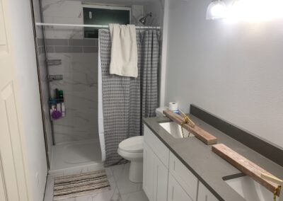 Remodeled basement bathroom with tiled shower, toilet, and wood vanity