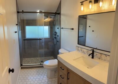 Remodeled bathroom with glass shower door, gray tile, wood vanity, and large mirror