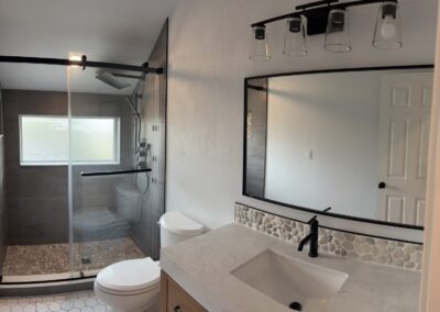 Remodeled bathroom with glass shower enclosure, black fixtures, and hexagon tile flooring