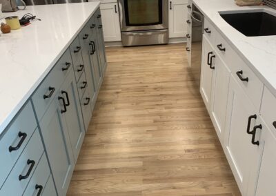View down a remodeled kitchen with white cabinets, blue-gray island, and stainless appliances