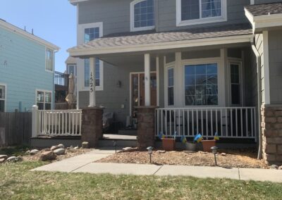 Two-story gray house with new covered front porch, white railing, and stone porch columns