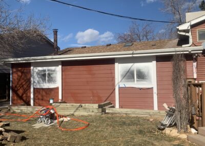 House exterior with red-brown lap siding being repainted and windows masked for painting