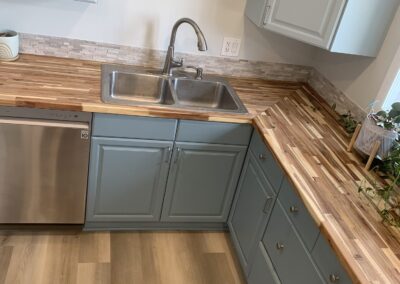 Remodeled kitchen corner with butcher block countertops, stainless sink, and stacked stone backsplash