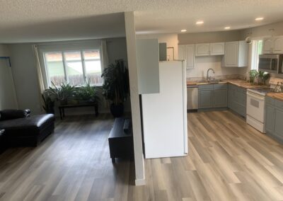 Open-concept living room and kitchen with white refrigerator, gray cabinets, and wood-look flooring