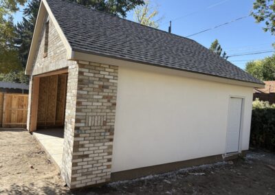 Close-up of detached garage with brick veneer corner, white stucco walls, and black roof