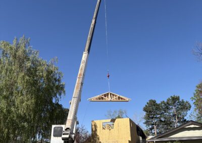 Crane lifting a roof truss onto a framed second-story home addition