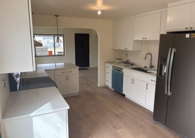 Remodeled white kitchen with stainless refrigerator, quartz counters, and wood-look flooring