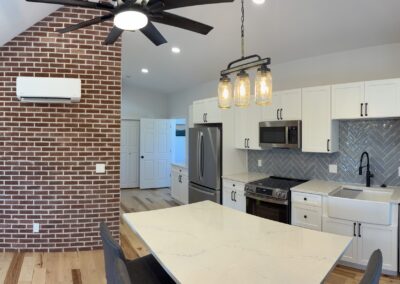 Remodeled kitchen with white cabinets, gray herringbone tile backsplash, and exposed brick accent wall
