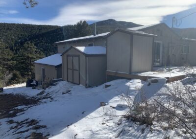Mountain home addition with tan siding, storage shed, and forested mountain views